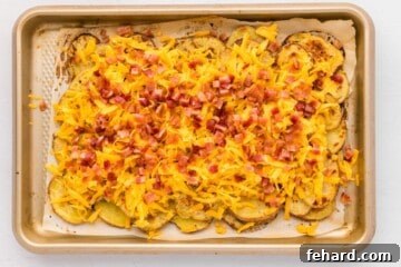 Baked potato slices layered on a baking sheet topped with shredded cheddar and bacon.