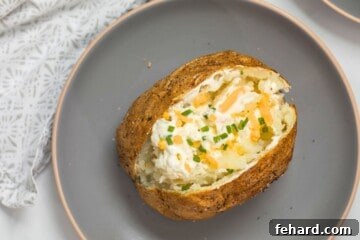 Air Fried Baked Potato on gray plate cut open and topped with dollop of butter, sour cream, cheddar, and pepper and chives.
