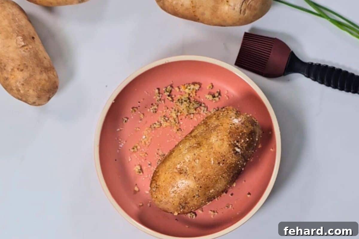 Baked Potato Air Fryer A single russet potato, perfectly coated in a savory mixture of garlic powder, kosher salt, black pepper, and olive oil, resting in a shallow dish, ready to be placed into the air fryer for cooking.
