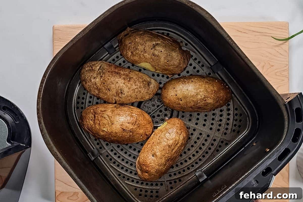 Potato skins placed skin side up in an air fryer basket after being brushed with seasoned butter, ready for initial air frying.