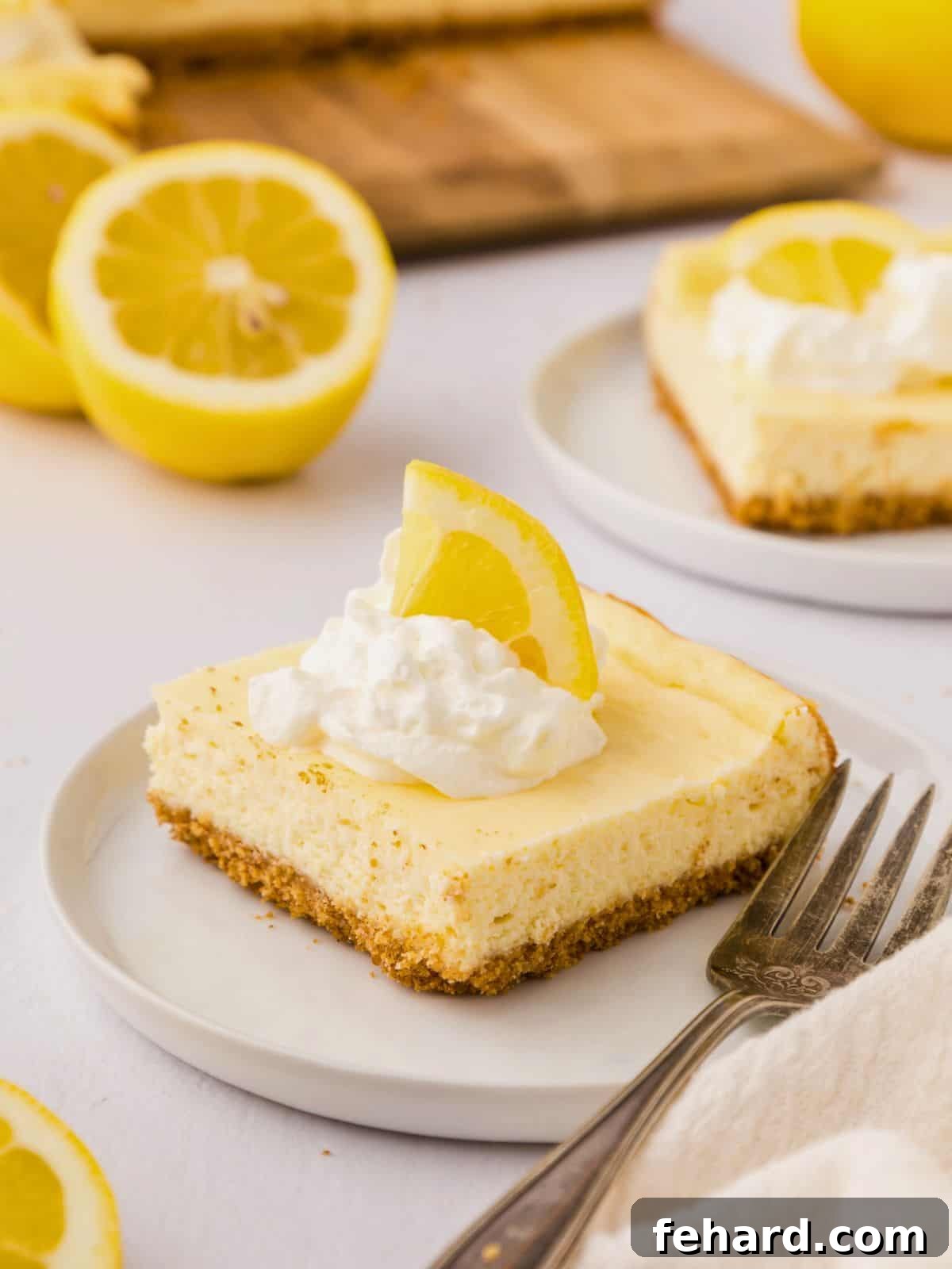 Lemon Cheesecake Bars One lemon cheesecake bar on white plate topped with whipped cream and a lemon wedge.