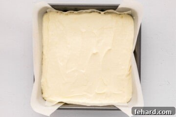 Zesty Lemon Cheesecake Bars 7 Cream cheese lemon batter spread evenly over graham cracker crust before baking.