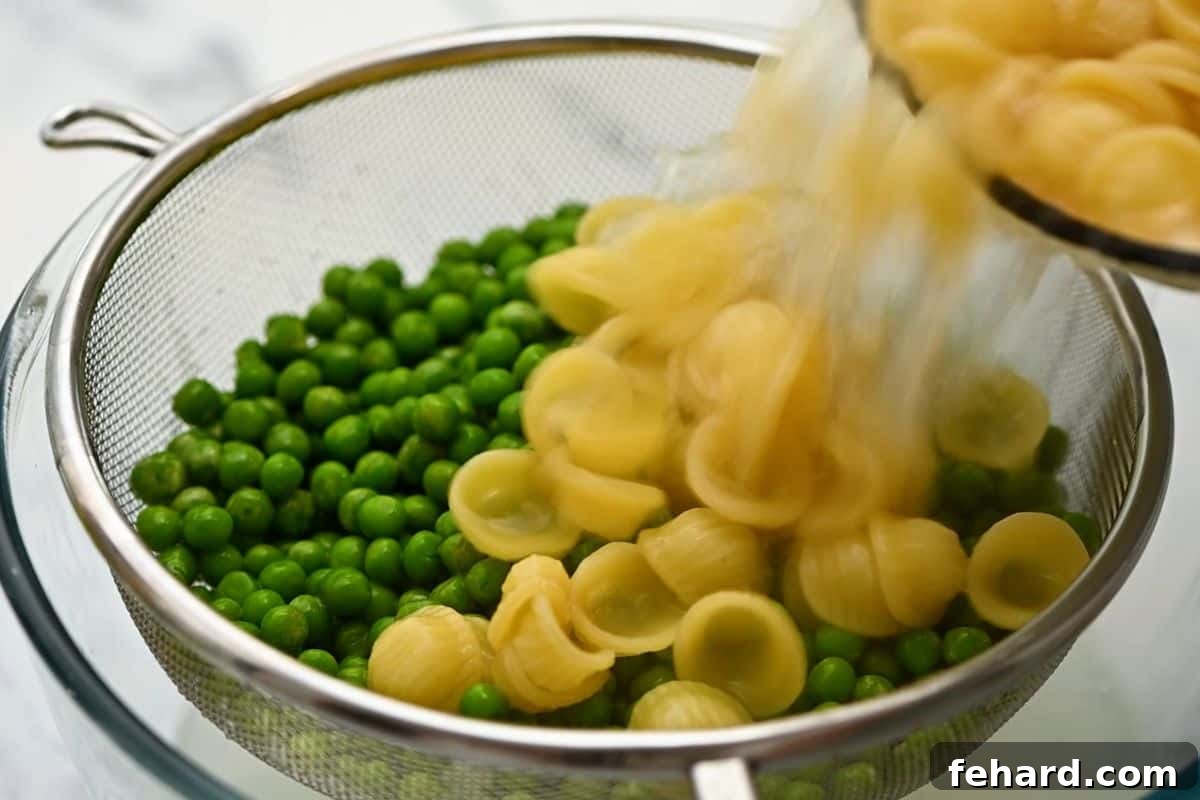 Draining Pasta Over Peas Hot, cooked pasta being carefully poured over a bed of fresh peas in a fine mesh colander, reserving the cooking water for the sauce.