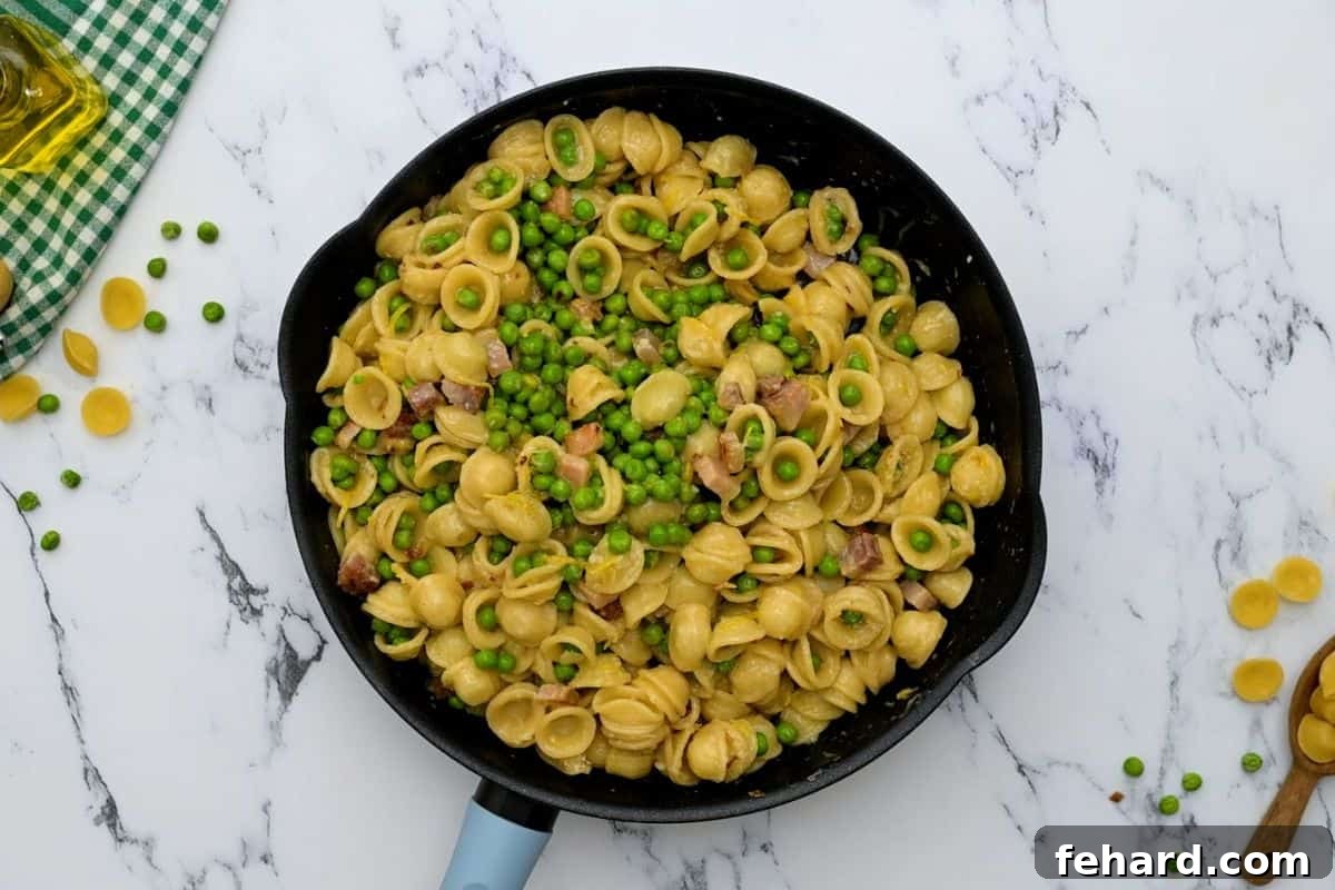 Finishing Pancetta Pasta with Peas A vibrant bowl of pasta with peas, pancetta, and Parmesan cheese, freshly tossed in a large skillet, ready to be served.