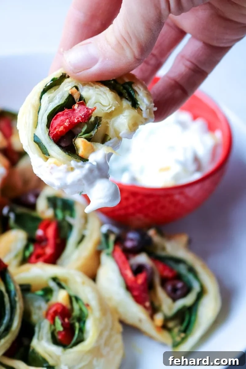 Greek Pinwheel Appetizer with Dip A Greek Pinwheel being dipped into a bowl of creamy Tzatziki Sauce.