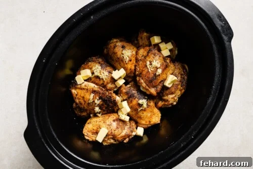 chicken thighs inside of a slow cooker with butter in top