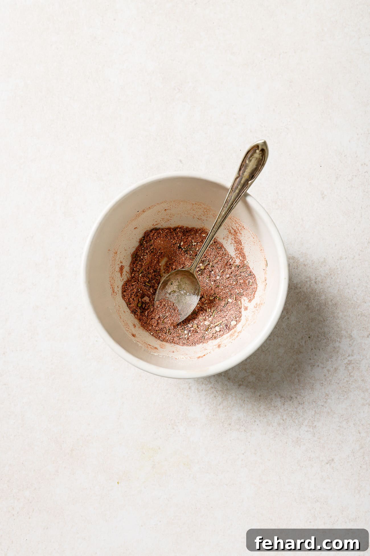 A small bowl of pre-mixed spices with a spoon in it. 