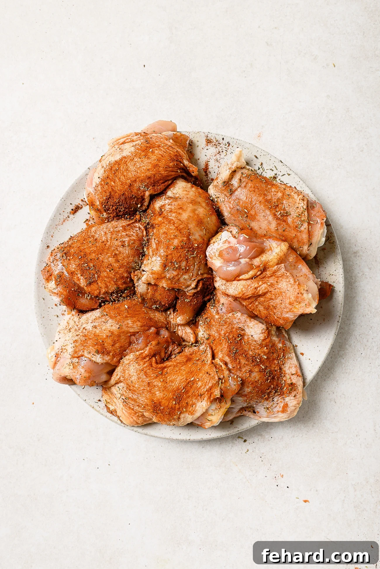 An overhead view of seasoned chicken thighs arranged on a white plate. 