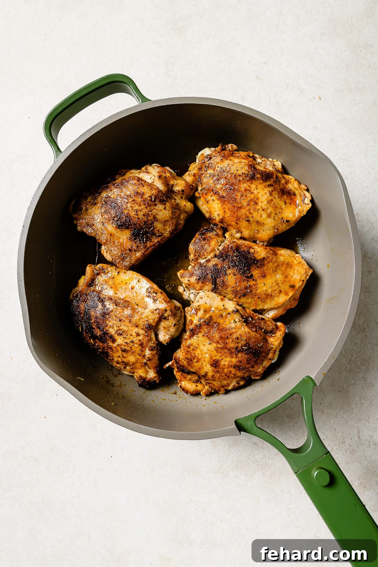 Five seared chicken thighs in a large cast iron skillet.