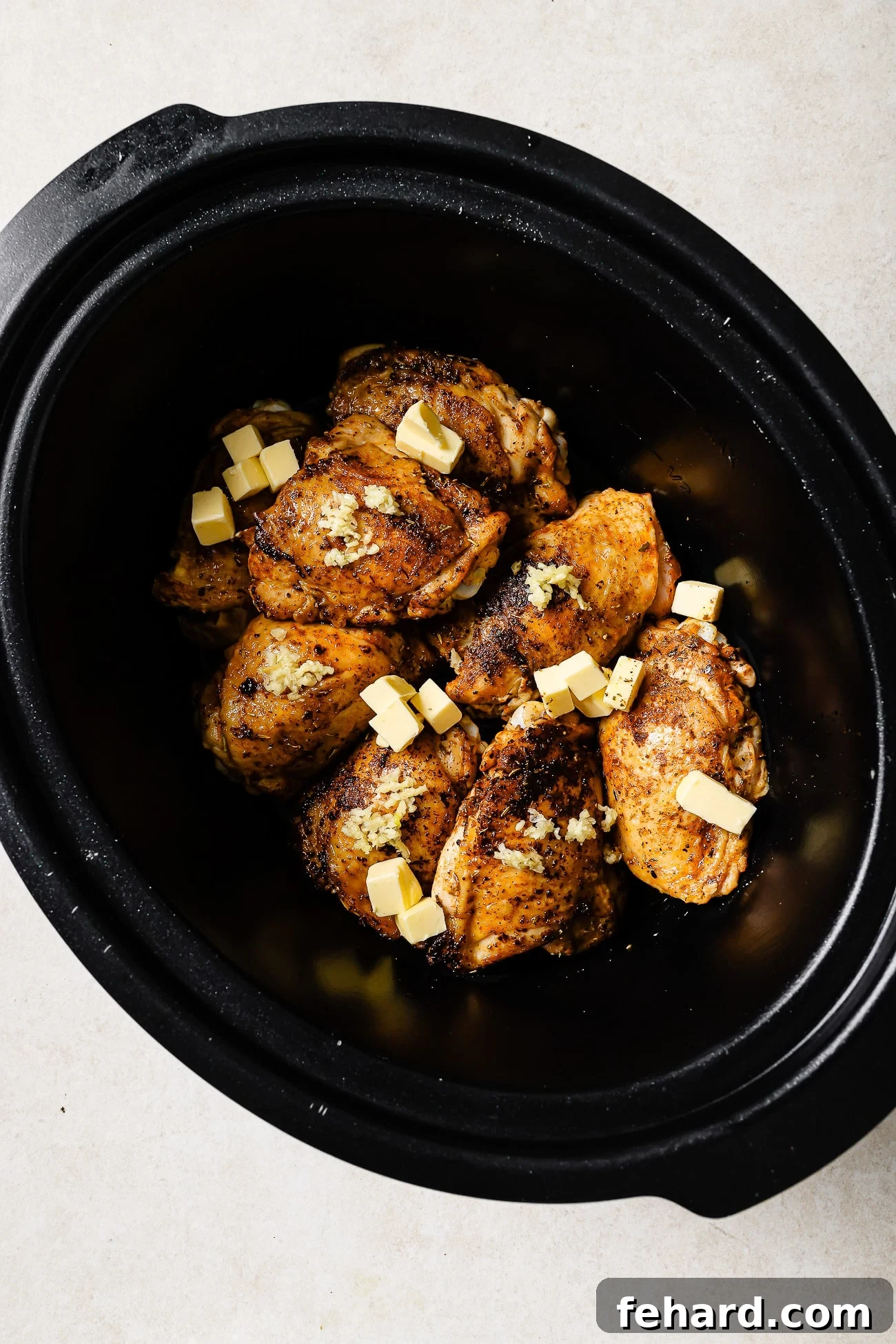 Seared chicken thighs in a slow cooker with butter and garlic on top. 