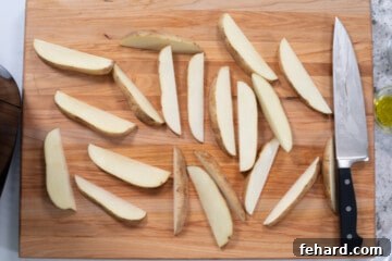 Sliced potato wedges on cutting board next to butcher's knife.