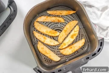Seasoned potato wedges in a single layer in the air fryer before air frying.