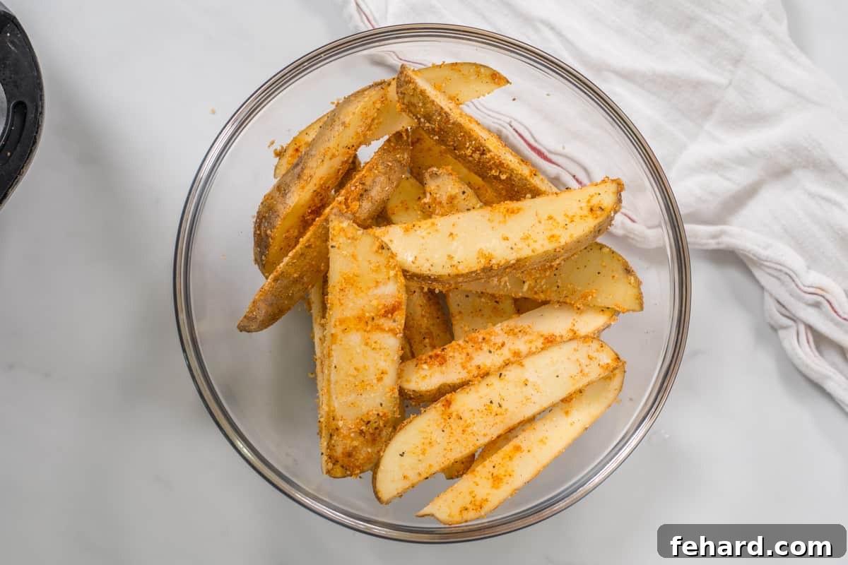 Mixing bowl with potato wedges coated in flour, parmesan, and seasonings.