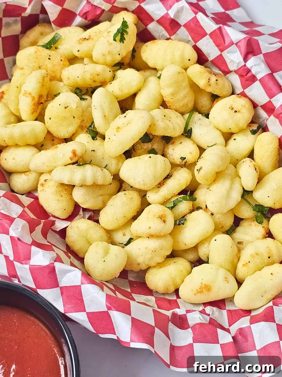 Air Fryer Gnocchi Basket with seasoned, crispy air-fried gnocchi served with marinara on the side.