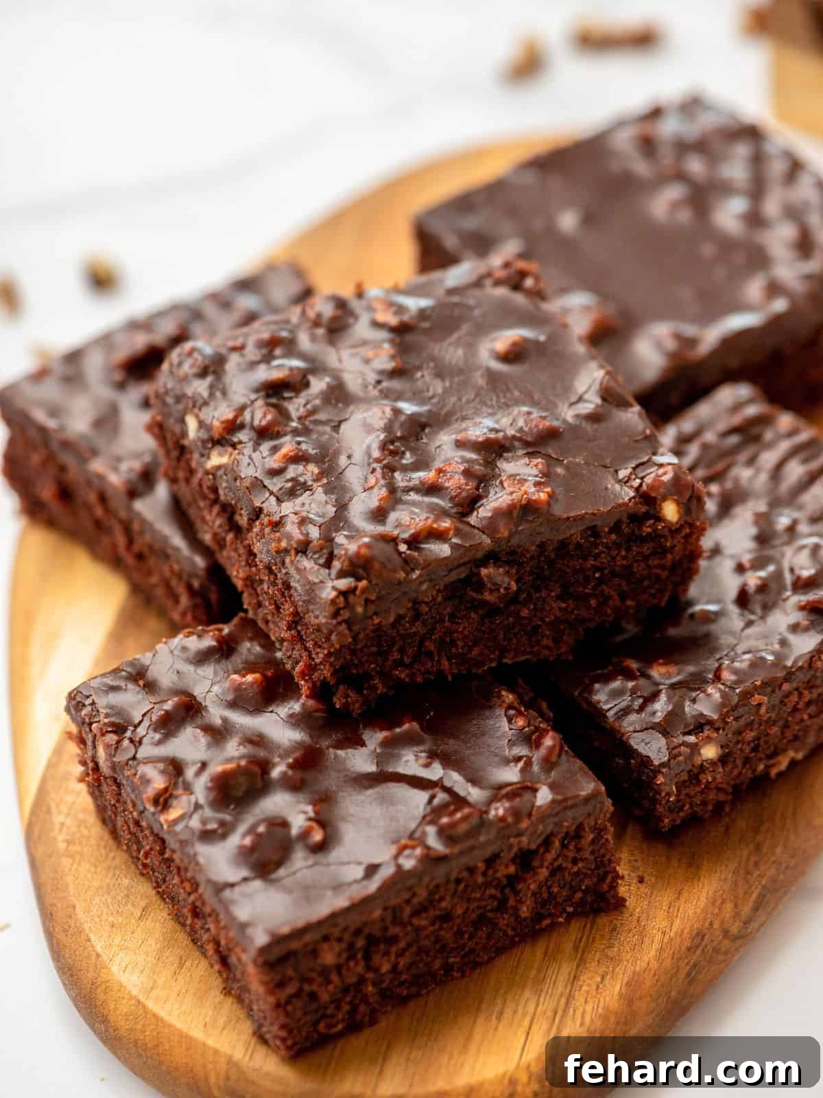 Sliced Texas sheet cake with pecans on wooden cutting board, showcasing its rich chocolate base and thick, fudgy frosting.