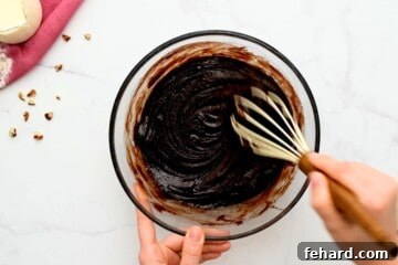 Hands whisking hot cocoa mixture into flour in a mixing bowl to cool the batter.