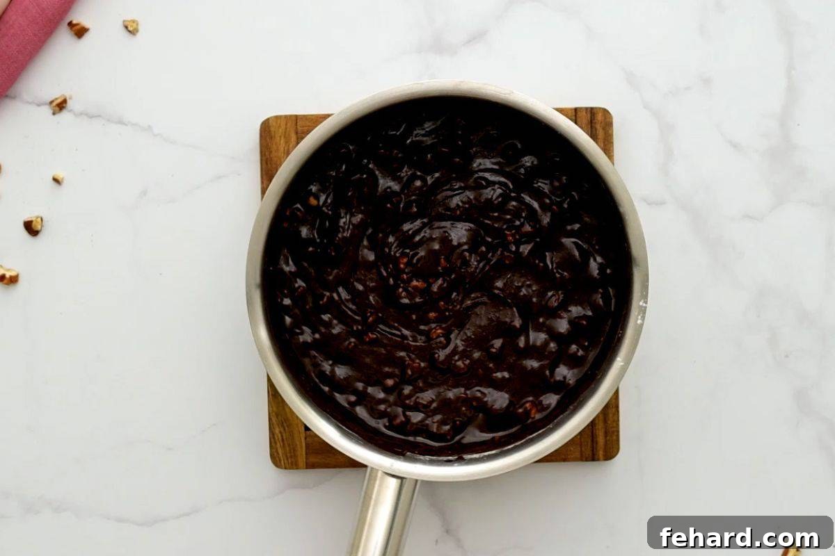 Saucepan with the rich, dark cocoa frosting after stirring in powdered sugar and nuts, ready to be poured.
