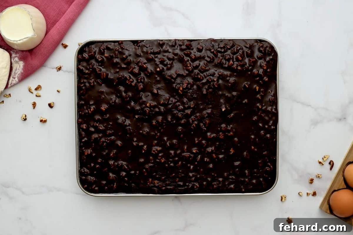 Pecan cocoa frosting being poured over a warm chocolate sheet cake in a pan, spreading beautifully.