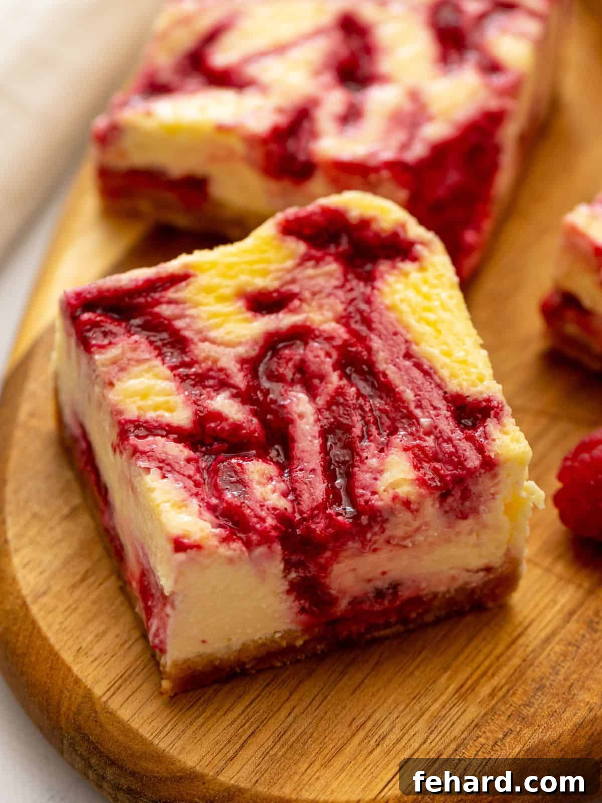 Sliced cheesecake bars on wooden cutting board revealing the raspberry swirl throughout the cheesecake batter.