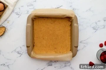 Graham Cracker crust pressed into an 8x8 baking dish lined with parchment paper with raspberries in background.