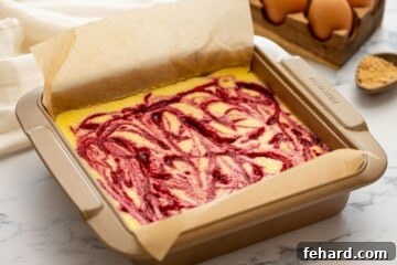 Swirled cheesecake bars in parchment lined baking dish.