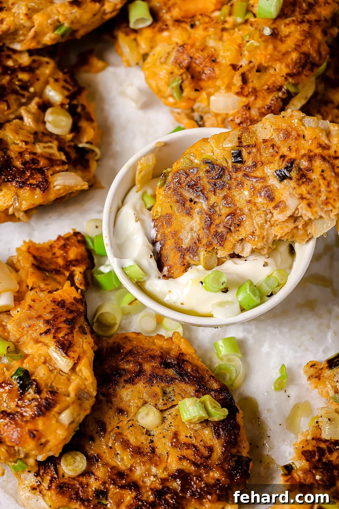 Close-up of a sweet potato tuna patty being dipped into a creamy sauce.