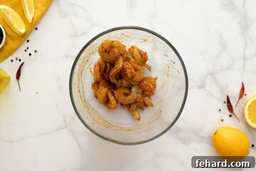 Raw shrimp being mixed with seasonings, olive oil, and fresh lemon zest in a bowl, showing thorough coating.