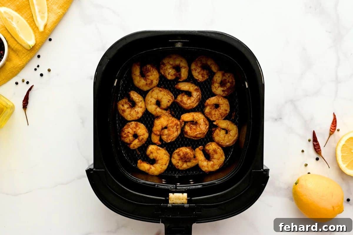 Perfectly arranged seasoned shrimp spread in a single, non-overlapping layer inside an air fryer basket, ensuring even cooking and crispiness.