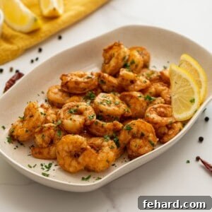 Platter of perfectly seasoned air fryer shrimp topped with fresh parsley and served with bright lemon wedges.