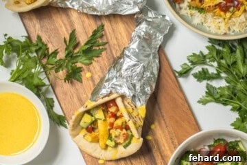 Grilled or pressure cooked Chicken shawarma in warmed pita with tomato cucumber topping and lemon tahini sauce on cutting board next to toppings.