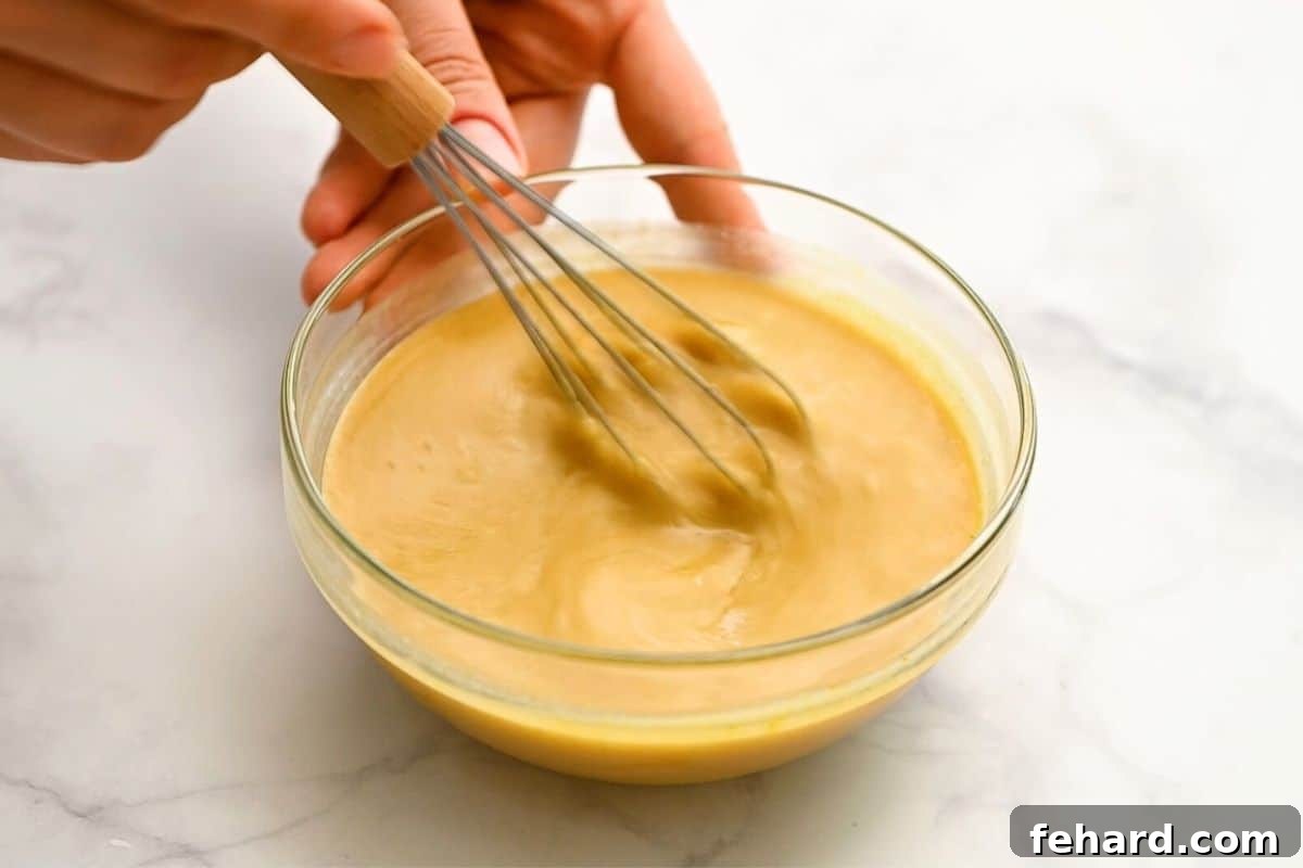 A whisk blending creamy lemon tahini sauce in a small glass bowl, showcasing its smooth, golden texture.