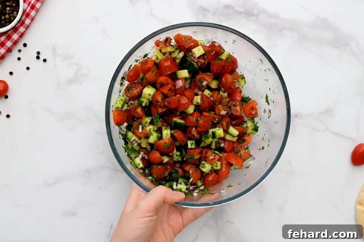 A fresh and colorful mix of diced tomatoes, cucumbers, minced red onions, and chopped parsley combined in a small mixing bowl, ready as a shawarma topping.