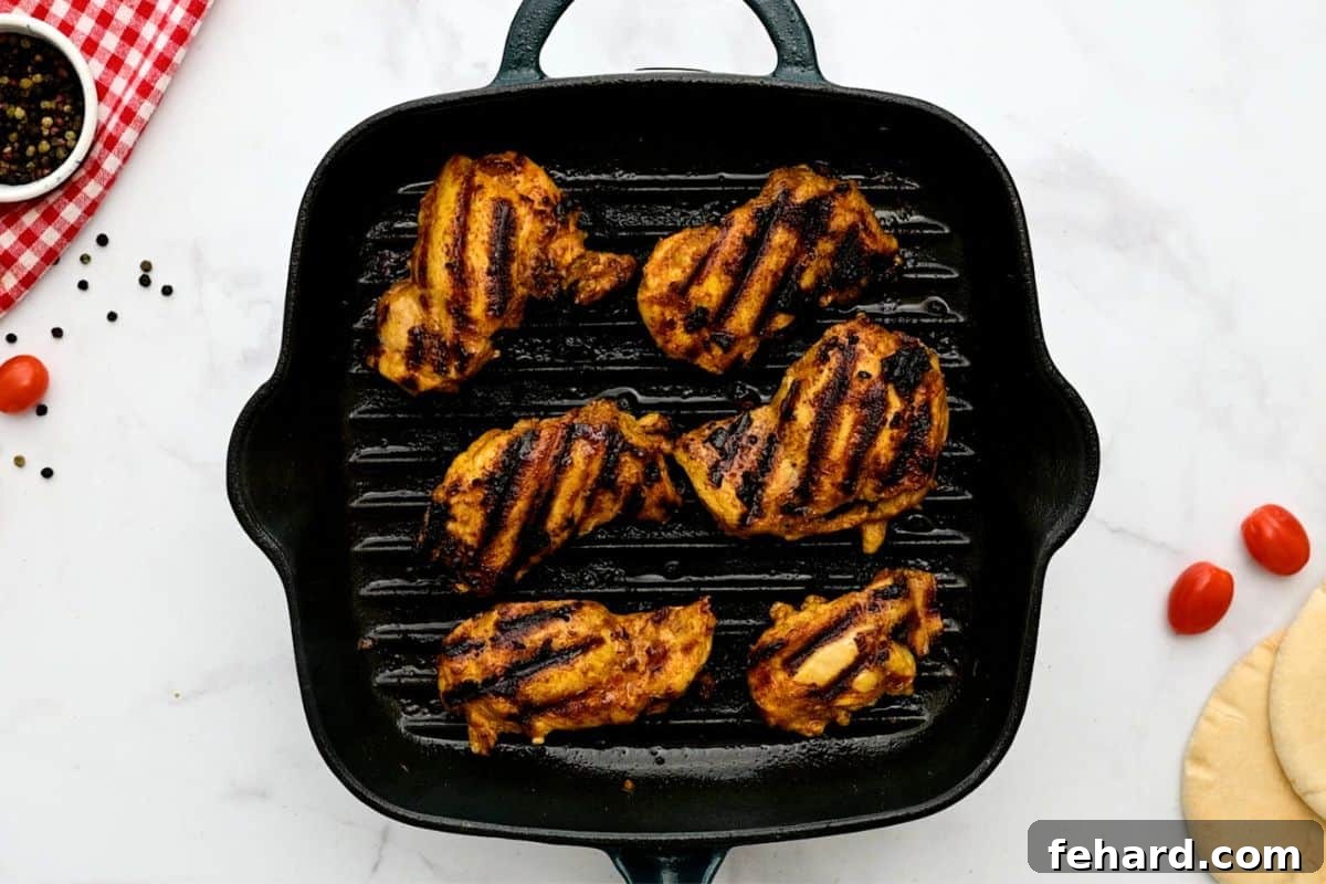 Marinated chicken thighs sizzling on a hot grill plate, showing beautiful browning and char marks.