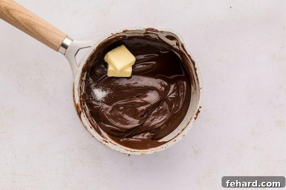 Easy Hot Fudge Sauce Saucepan with melted chocolate and condensed milk, with butter and salt added in, being stirred.