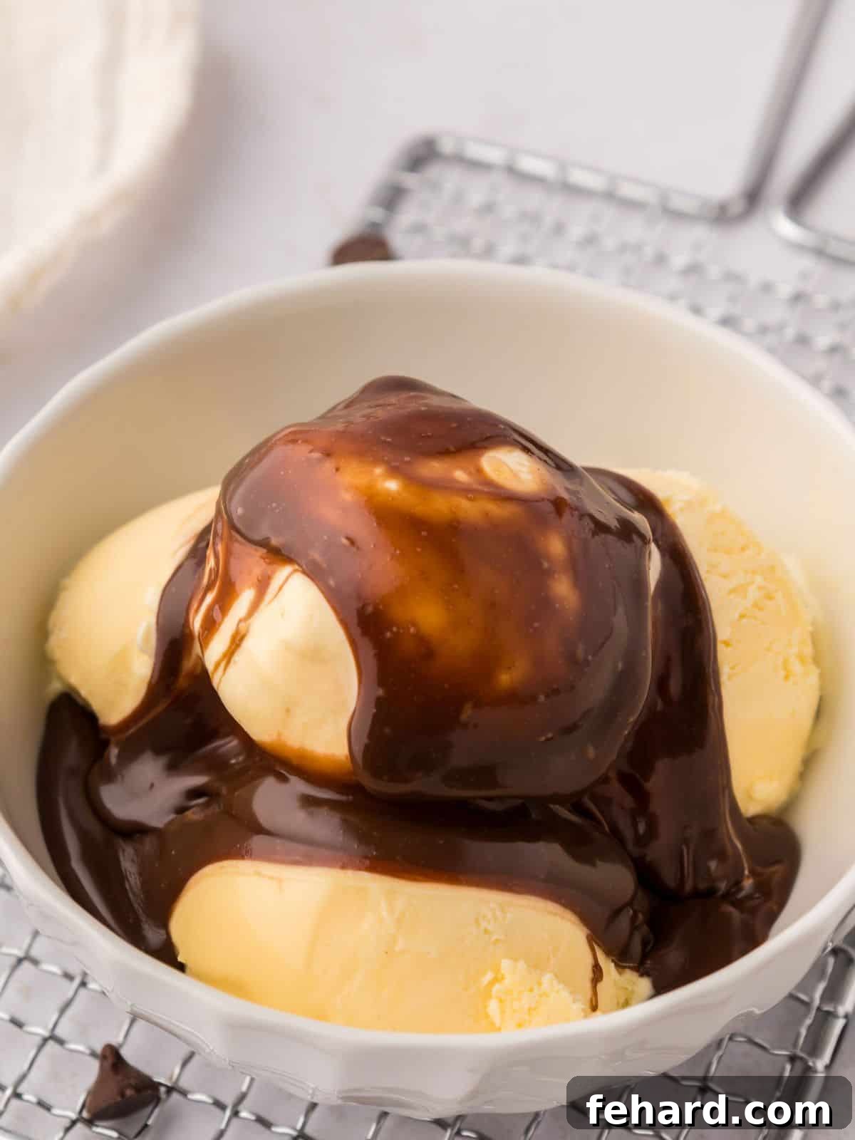 Homemade Hot Fudge Recipe A bowl of creamy vanilla ice cream generously drizzled with warm, homemade hot fudge sauce.