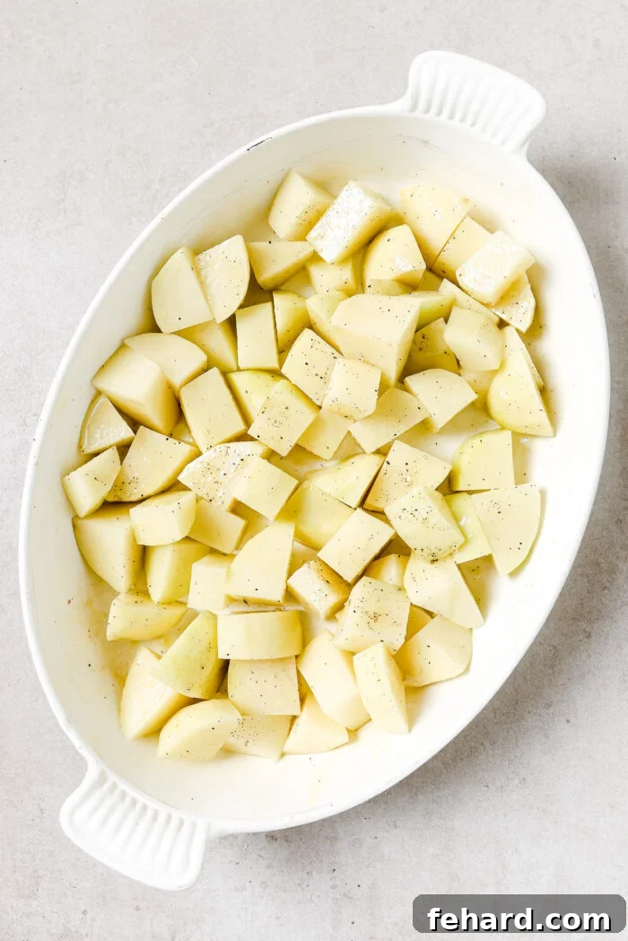 Diced potatoes seasoned with salt and pepper in a white oval baking dish.