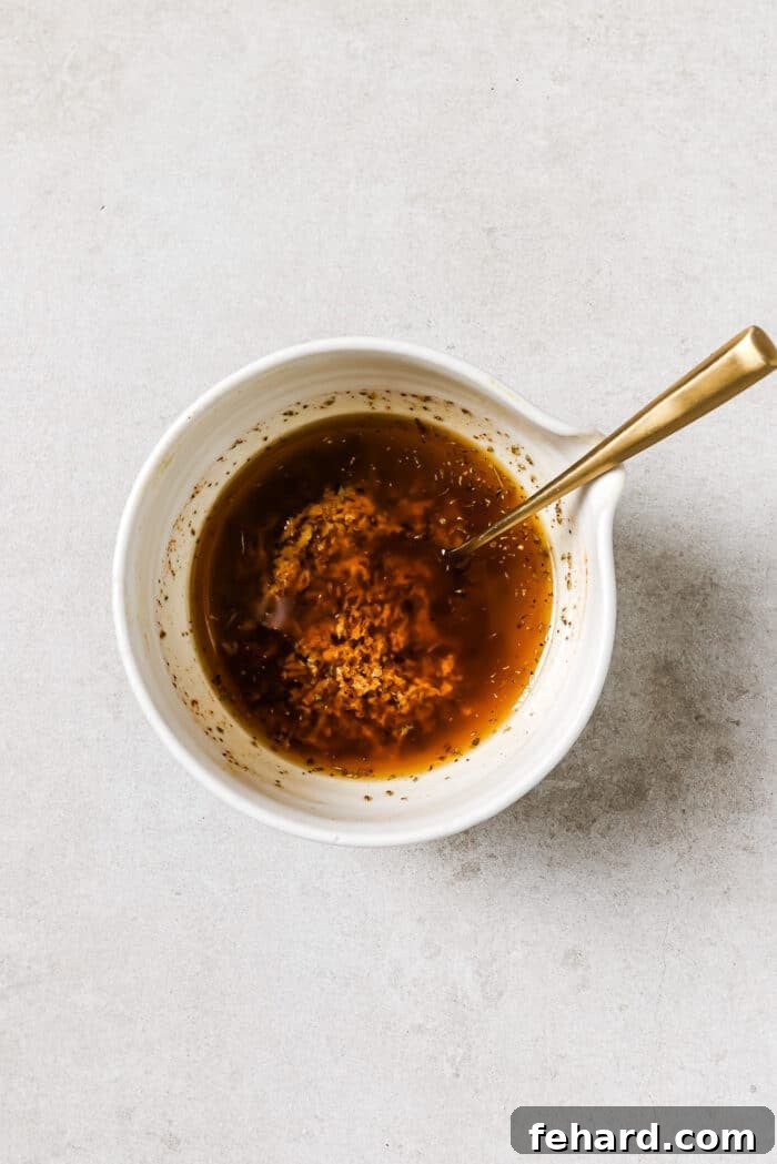 Greek chicken marinade in a white mixing bowl with a gold spoon in it.