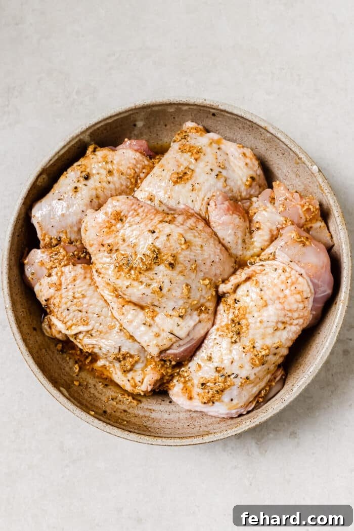 An overhead view of marinated chicken thighs in a large mixing bowl.
