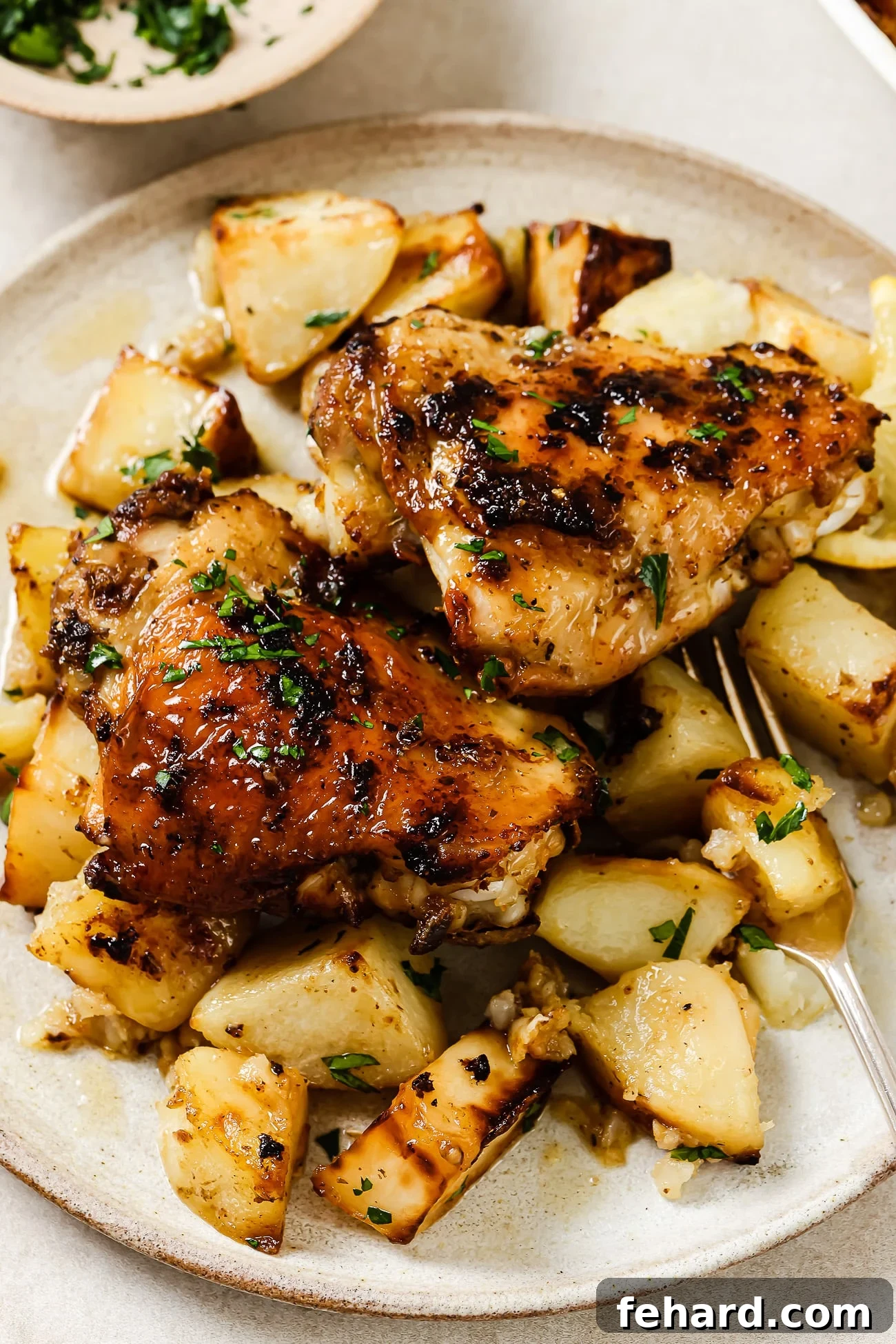 Two Greek chicken thighs over a bed of roasted potatoes on a white plate.