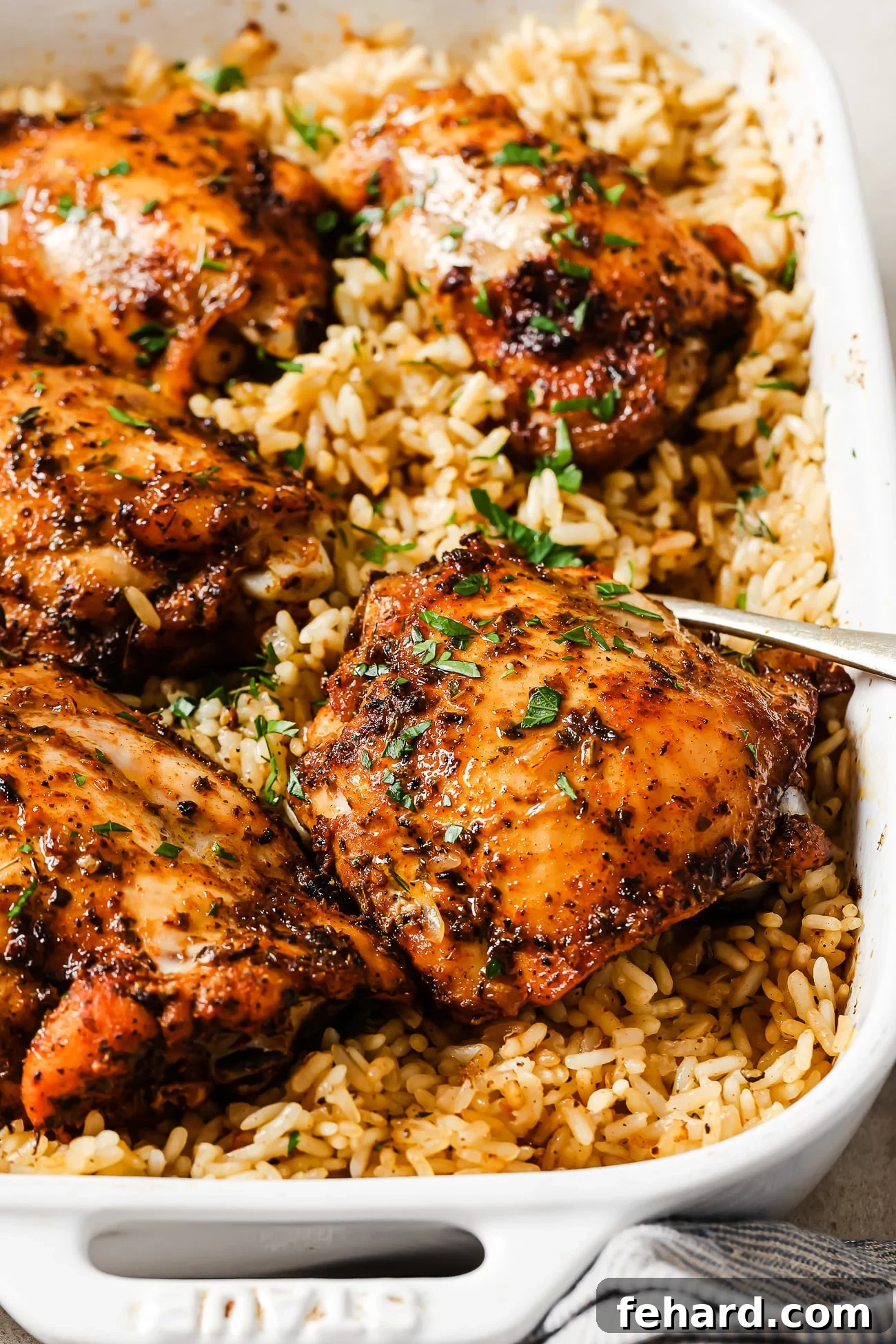 An overhead view of golden-brown baked chicken and rice in a white casserole dish, garnished with fresh herbs.