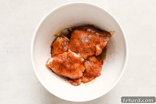 Raw chicken thighs in a white bowl, coated in spices and olive oil.