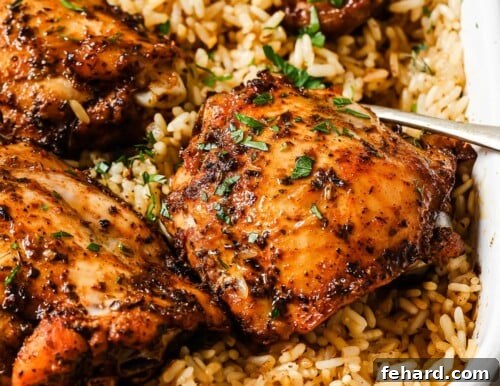Close-up of baked chicken thighs over fluffy rice in a white casserole dish, ready to be served.