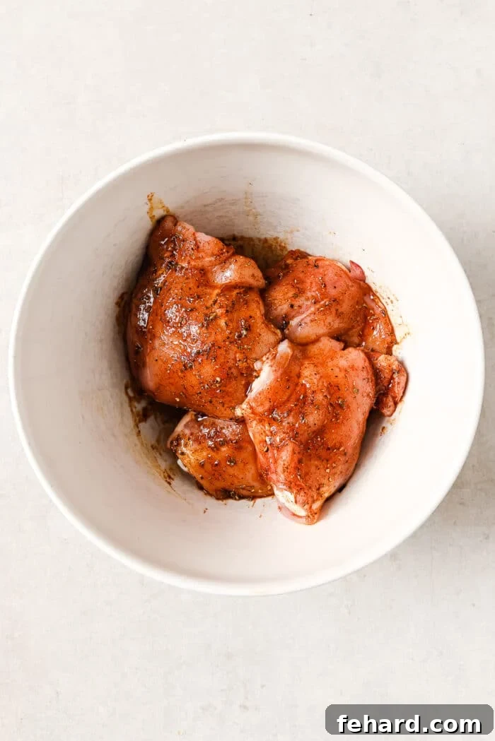 An overhead view of marinated chicken thighs coated in spices, resting in a white serving bowl.