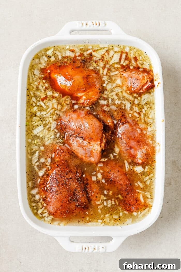 Six marinated chicken thighs carefully arranged and nestled into the uncooked rice, garlic, and onion mixture in a white casserole dish.