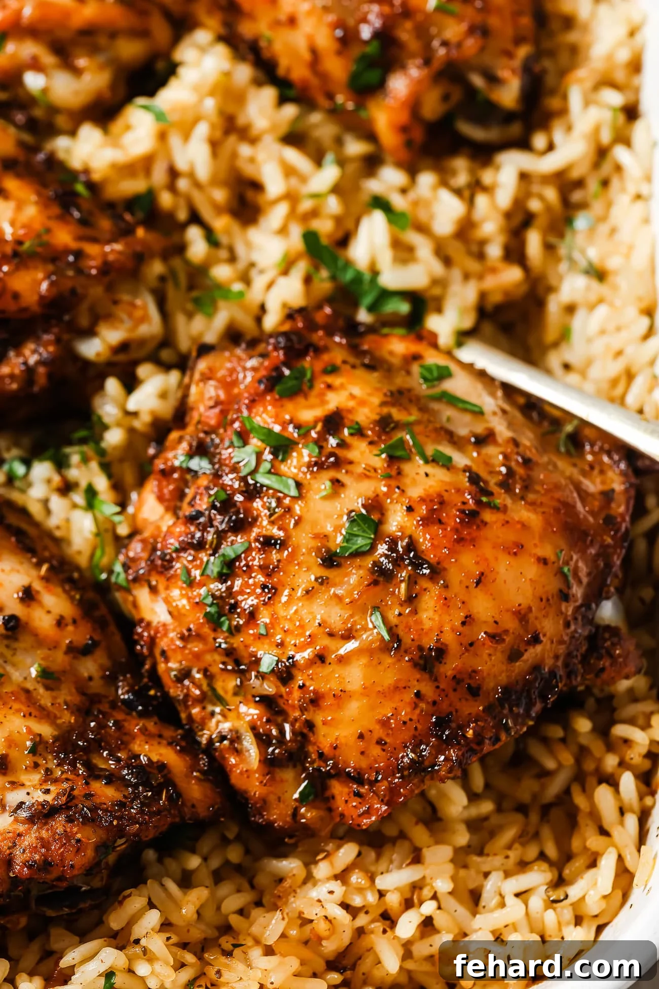 A close-up shot of perfectly baked chicken thighs resting on a bed of fluffy, seasoned rice in a white baking dish, garnished with fresh herbs.