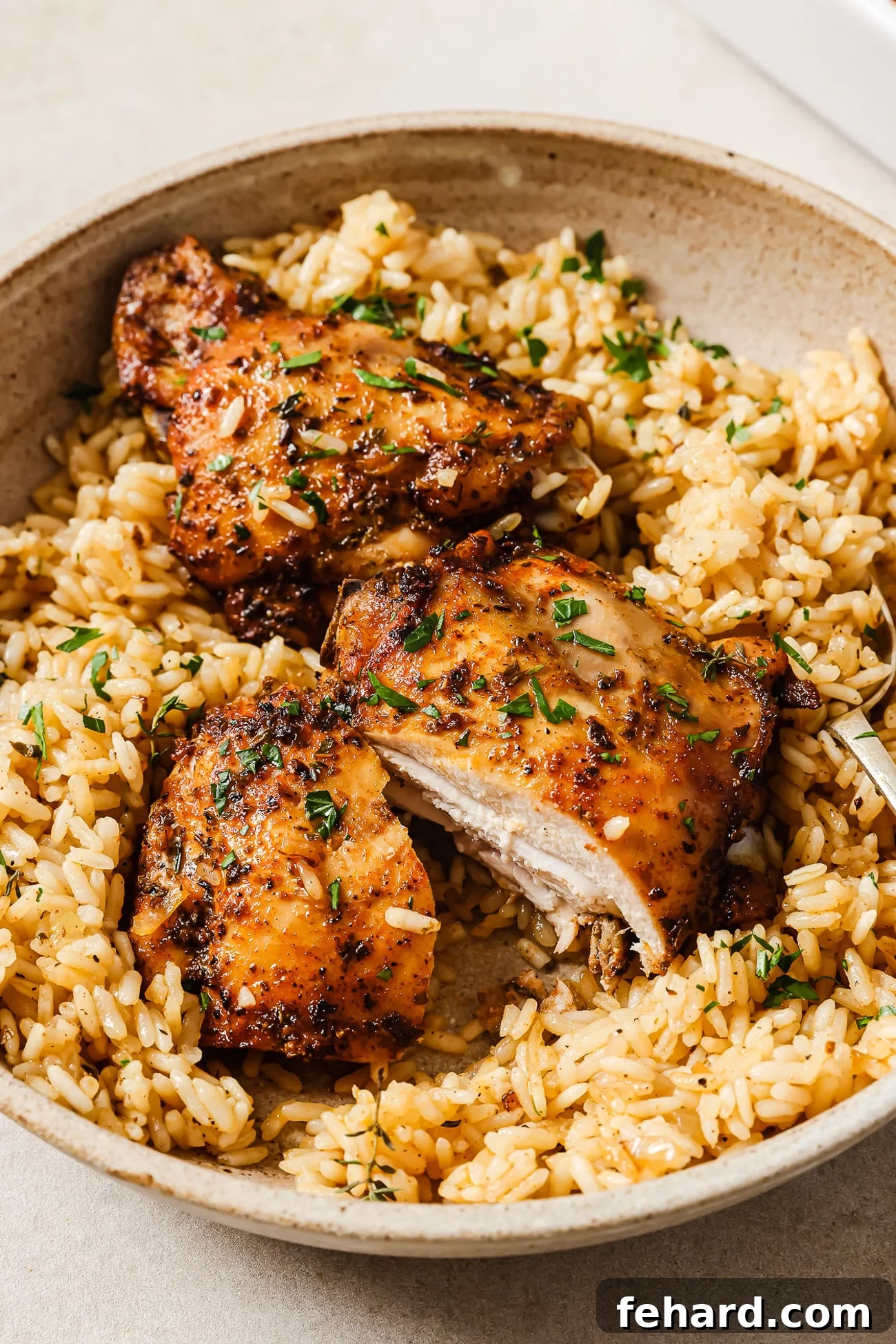 Two beautifully baked chicken thighs served over a portion of fluffy rice in a white serving bowl, garnished with fresh parsley.