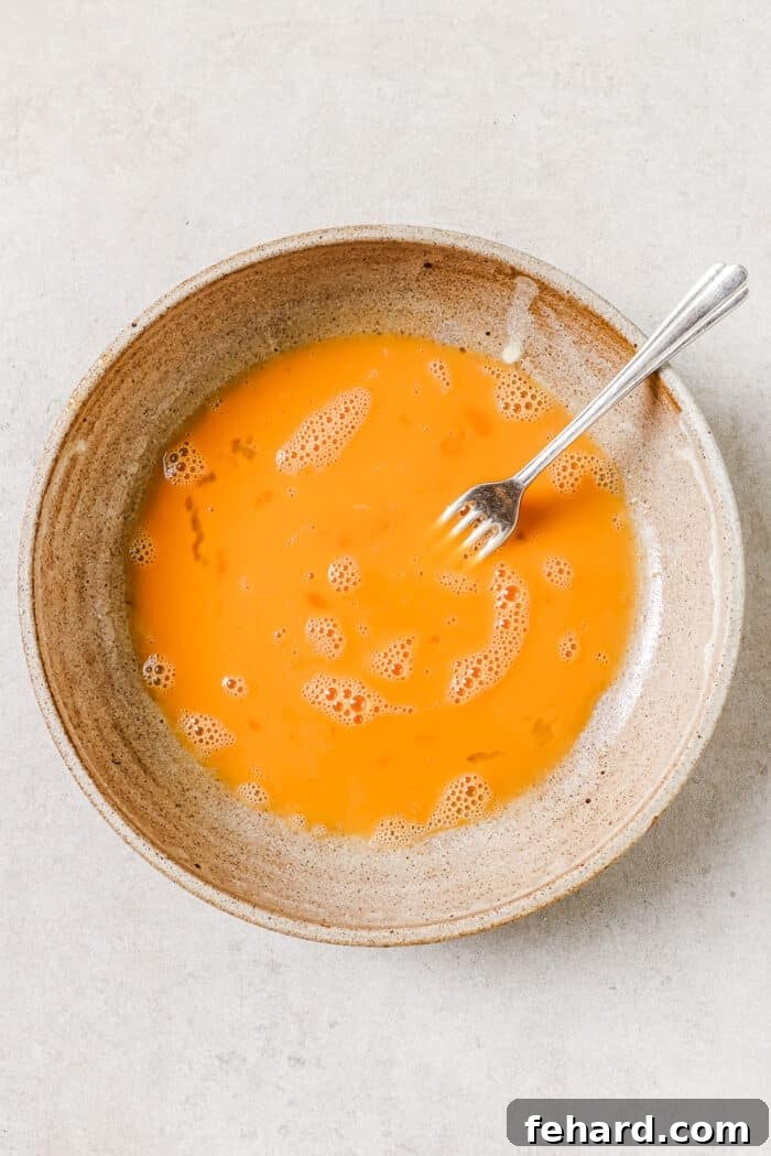 An overhead view of eggs beaten in a mixing bowl with a fork resting on the side of it.