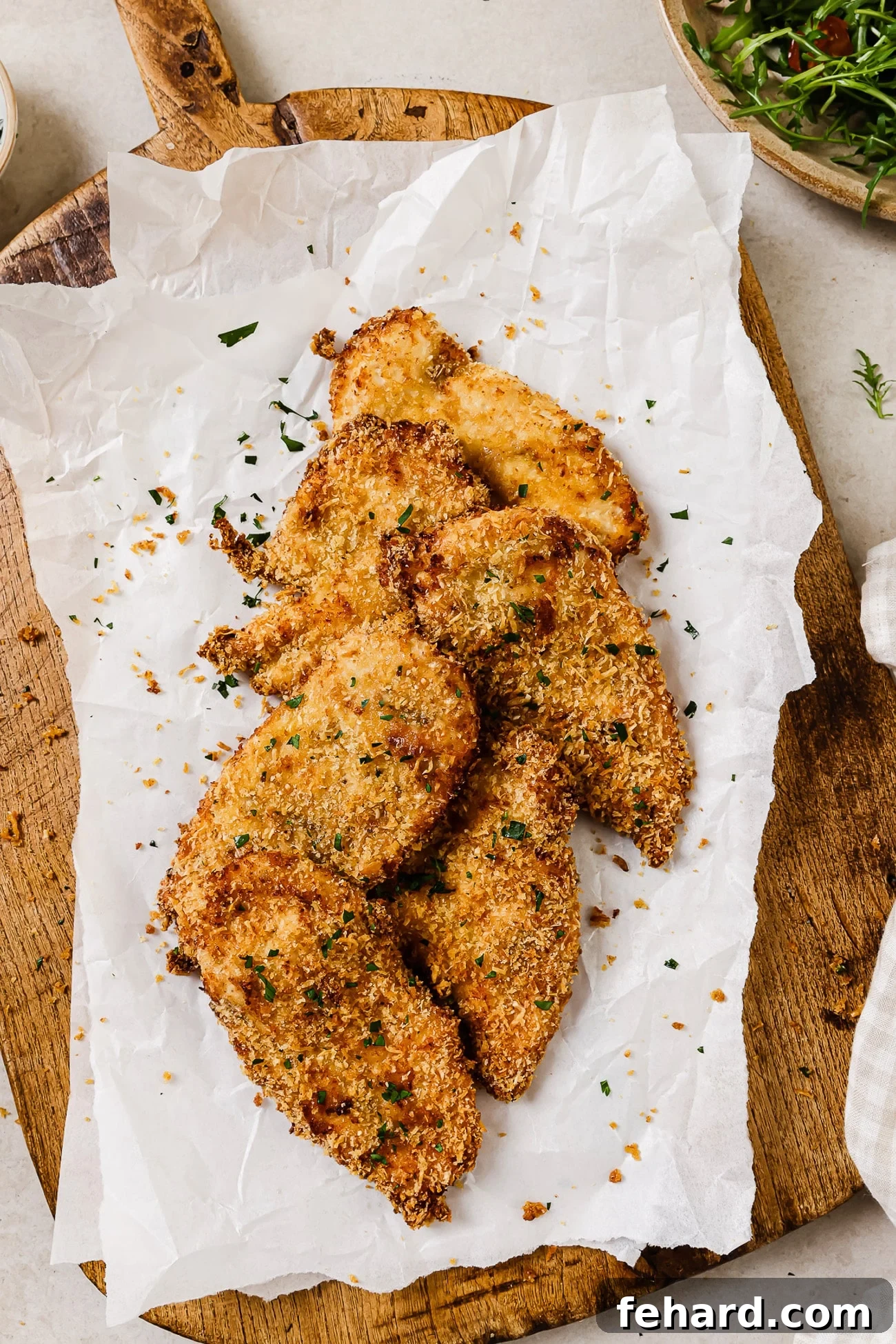 An overhead view of air fryer chicken cutlets on parchment paper and a cutting board, ready to serve.
