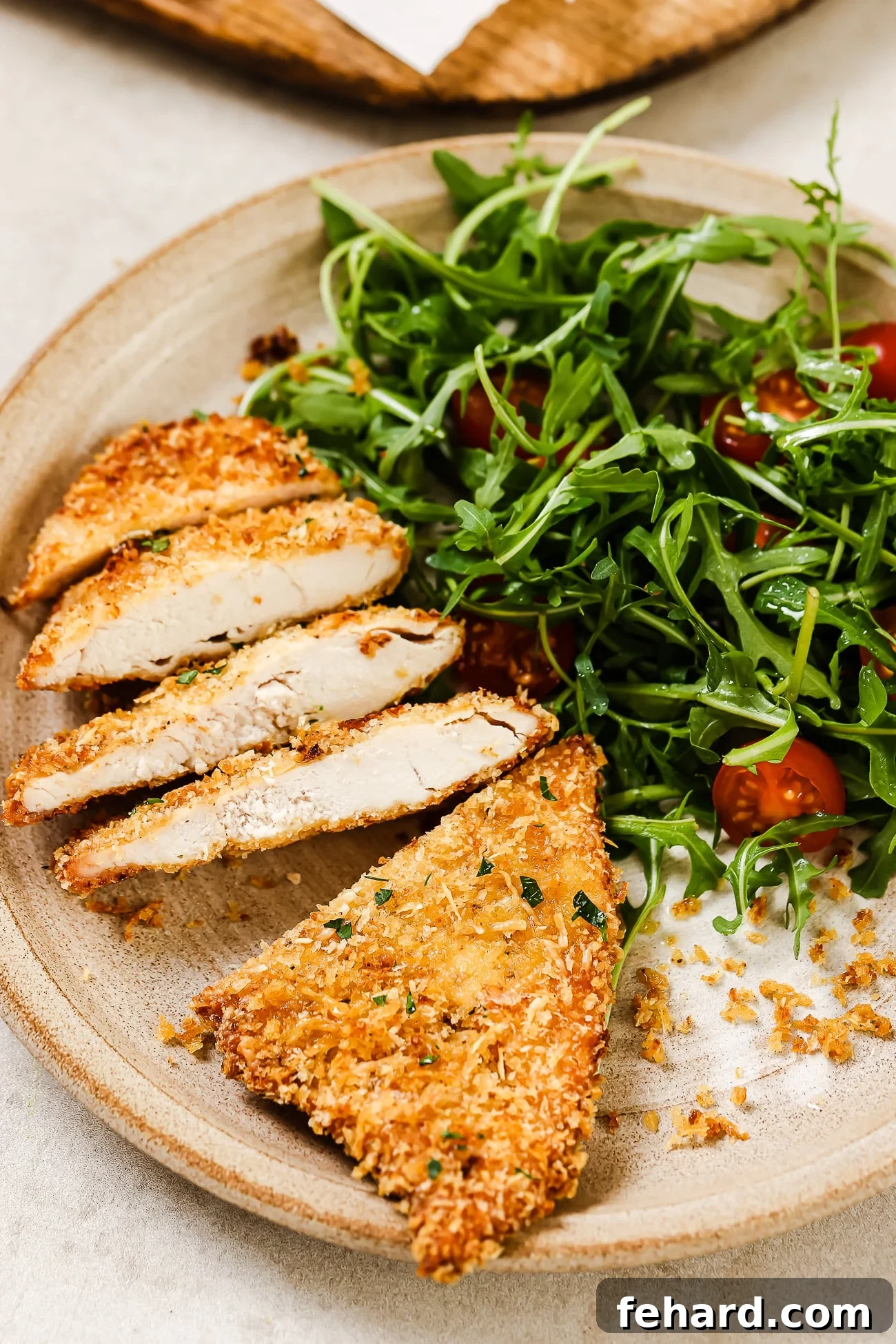 A sliced air fryer chicken cutlet on a plate with a vibrant side salad, showcasing its crispy exterior and juicy interior.