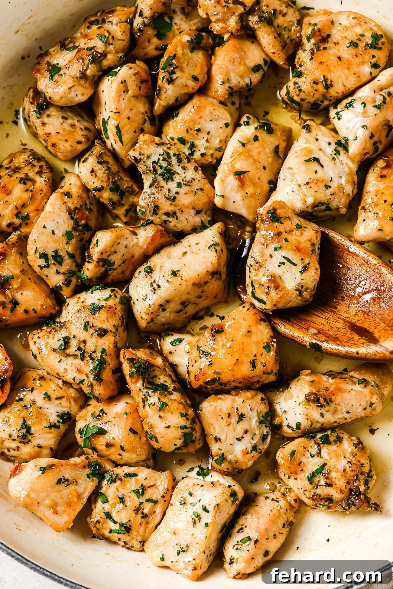 Closeup of perfectly cooked, golden-brown chicken bites glistening in a white skillet, ready to be served.
